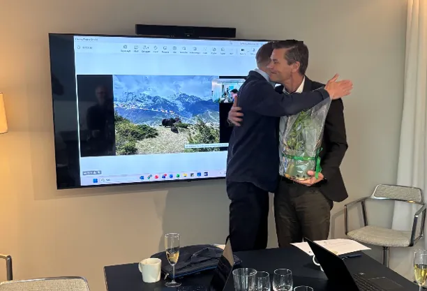 Två personer kramas vid MobiOnes closingceremoni, framför en skärm som visar ett bergsfoto